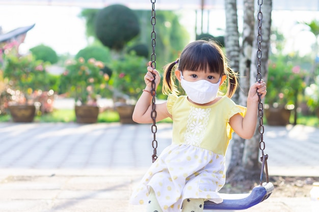 Muchacha asiática del niño que lleva una máscara facial de la tela cuando ella juega un juguete en el patio.