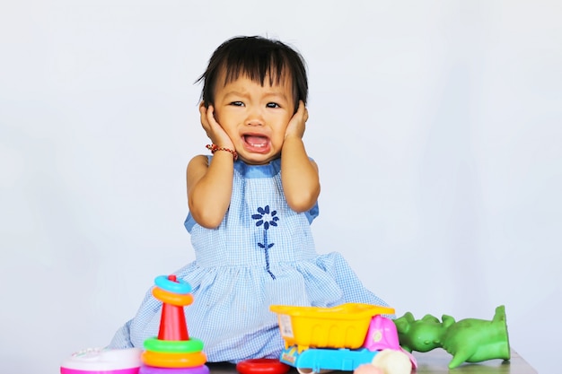 Muchacha asiática del niño que llora y que juega con muchos juguetes.