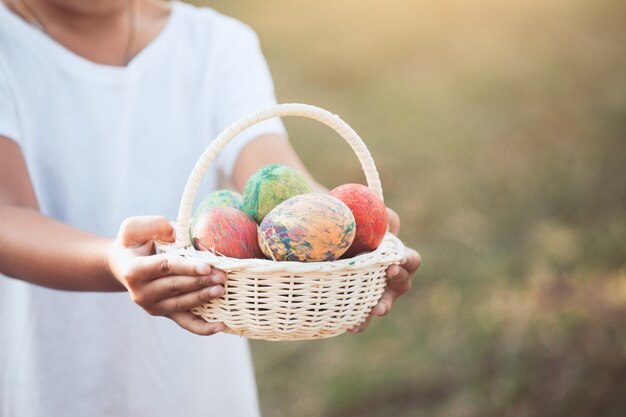 Muchacha asiática del niño que sostiene la cesta con los huevos de Pascua coloridos