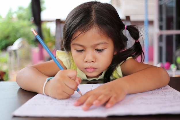 Muchacha asiática del niño uso Lápiz escribe letras en el libro