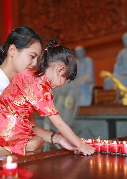 La muchacha asiática del niño en vestido tradicional enciende las velas de la adoración en el templo chino