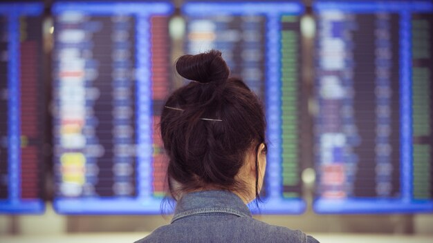 Muchacha asiática que mira el horario de vuelo en la terminal de aeropuerto, solo concepto del viajero