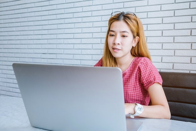 Muchacha asiática que trabaja en una cafetería que se sienta con el teléfono móvil y la computadora portátil.