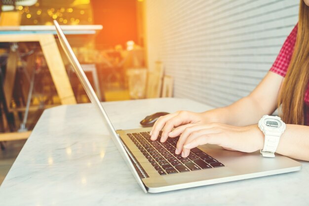 Muchacha asiática que trabaja en una cafetería que se sienta con el teléfono móvil y la computadora portátil.