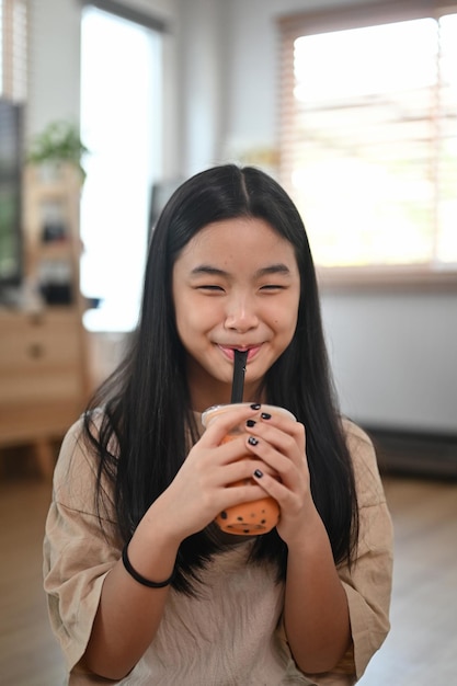 Muchacha asiática sonriente que bebe té helado de la leche de la burbuja.