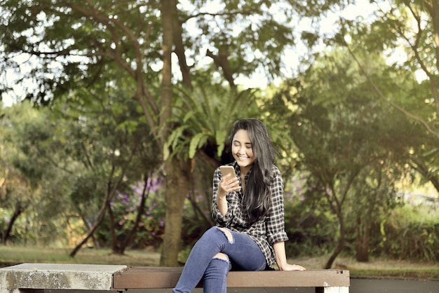 Foto muchacha asiática sonriente con la sentada del teléfono móvil