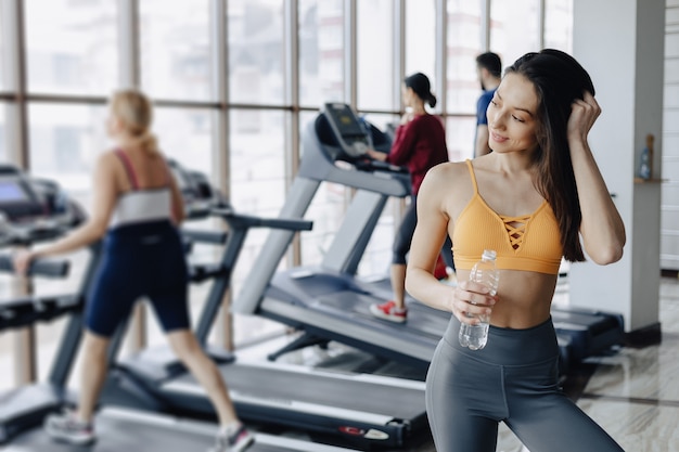 Muchacha atractiva joven en el agua potable del gimnasio en el fondo de cintas de correr