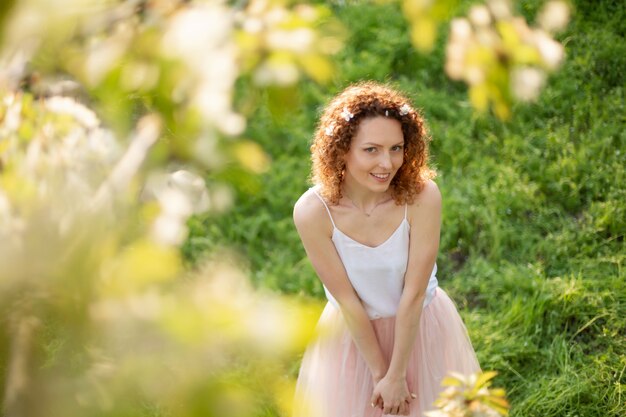 La muchacha atractiva joven camina en el parque verde de la primavera que disfruta de la naturaleza floreciente