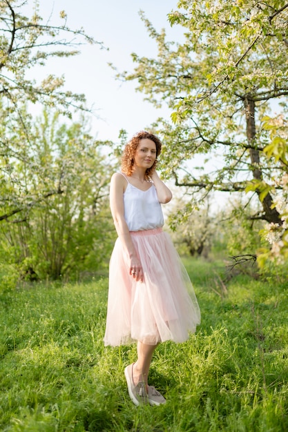 La muchacha atractiva joven camina en el parque verde de la primavera que disfruta de la naturaleza floreciente