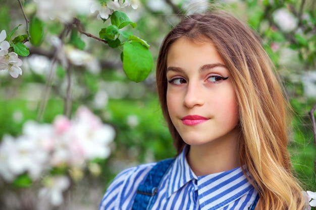 La muchacha bastante adolescente está planteando en el jardín cerca del árbol en flor con flores blancas. Tiempo de primavera