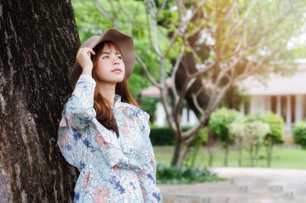 Muchacha bastante asiática en el vestido de la vendimia que se inclina contra en el árbol y que se relaja.