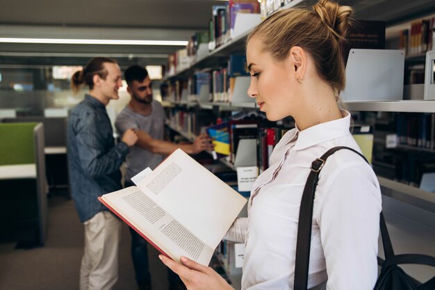 La muchacha bastante pensativa se parece al estudiante que se coloca con el libro en la biblioteca de una universidad