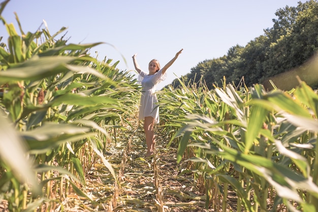 Muchacha de la belleza en el campo de maíz del verano sobre el cielo azul claro. Feliz joven sana disfrutando de la naturaleza al aire libre. Mujer corriendo y girando. Volador. Libre, concepto de libertad, medio ambiente.