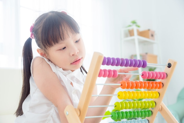 Muchacha bonita asiática que cuenta la madera en el ábaco en casa. Concepto de educación infantil.