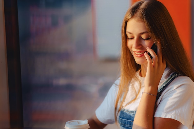 La muchacha bonita atractiva joven en el café con café y el teléfono en la mañana emite