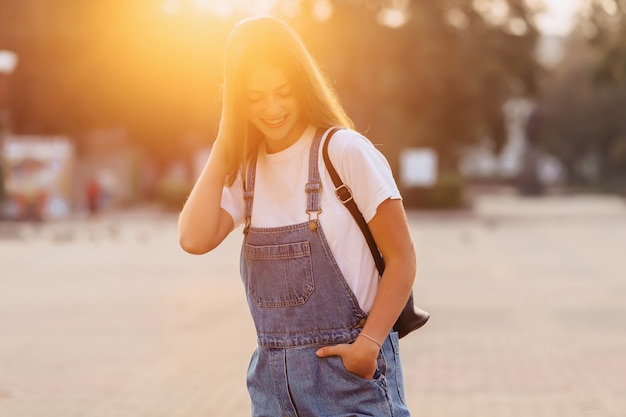 La muchacha bonita atractiva con el maletín camina en la calle en las luces de la salida del sol de la mañana