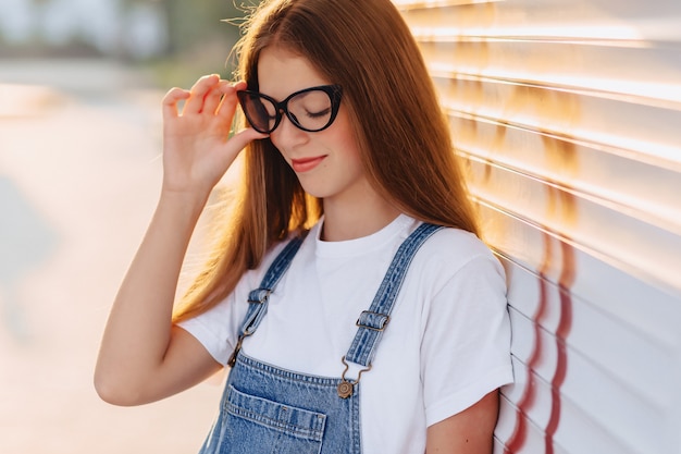 Muchacha bonita atractiva positiva joven en vidrios elegantes en la sol de la mañana