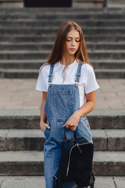 Muchacha bonita joven con el paseo de la cartera en la calle cerca del edificio