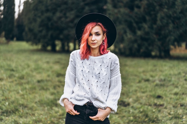 Muchacha bonita con el pelo rojo y el sombrero que se relaja en el parque, tiempo de otoño.