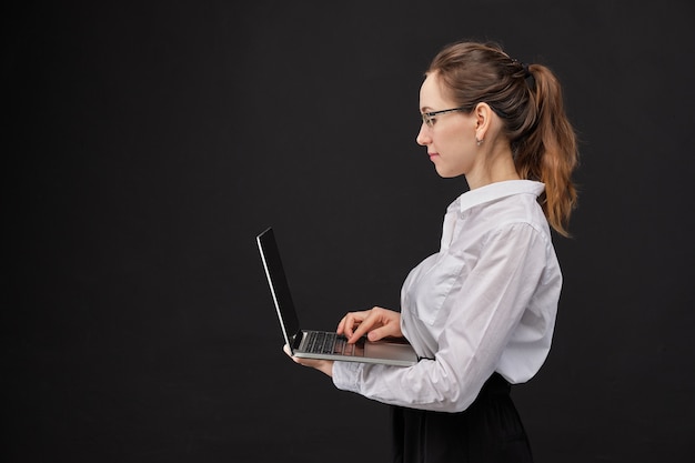 Muchacha en una camisa blanca que sostiene una computadora portátil en un fondo negro.