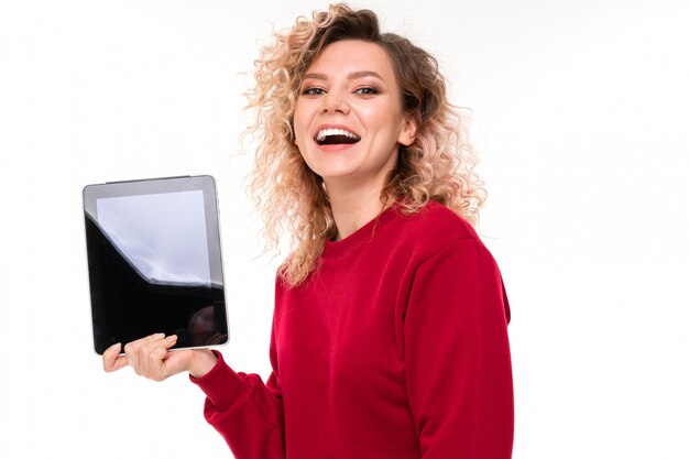 La muchacha caucásica con el pelo rubio rizado sostiene una tableta y sonríe, retrato aislado