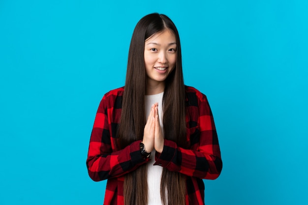 Foto la muchacha china joven en azul aislado mantiene la palma unida. la persona pide algo