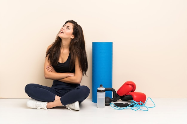 Muchacha del deporte del adolescente que se sienta en el piso feliz y que sonríe