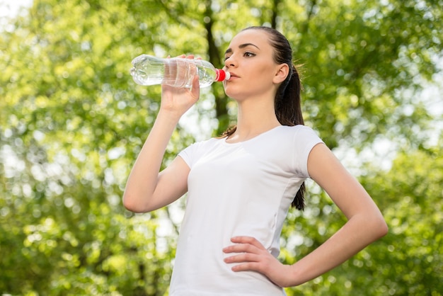 Muchacha deportiva hermosa en el agua potable de la camiseta blanca.