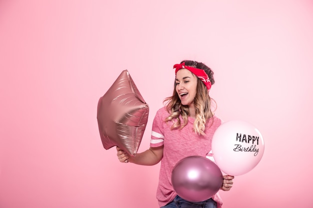 Muchacha divertida en una camiseta rosa con globos Feliz cumpleaños da una sonrisa y emociones en una pared rosa