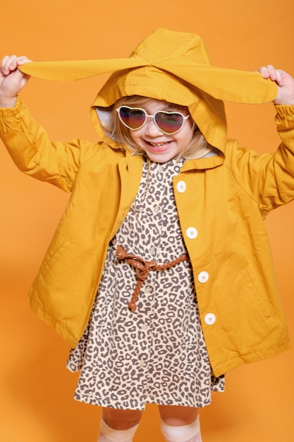 Foto muchacha divertida en impermeable amarillo con orejas de conejo sobre fondo amarillo