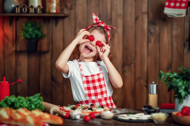 Muchacha divertida que cocina la pizza y que engaña con los tomates