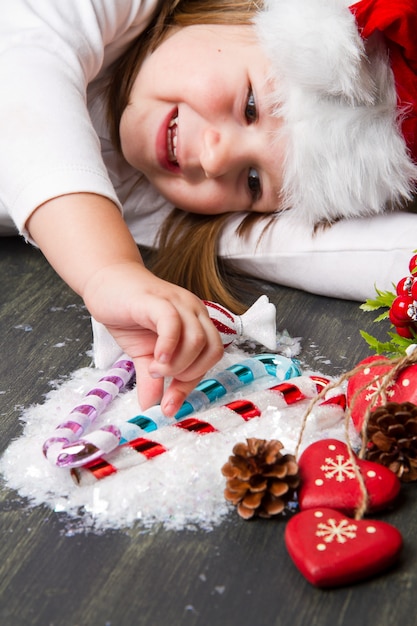 Muchacha divertida en el sombrero de Santa escribe carta a Santa cerca de decoración navideña