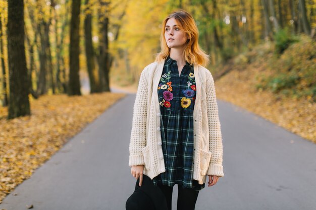 La muchacha elegante del hippie en un suéter y un sombrero hechos punto camina en el parque del otoño.