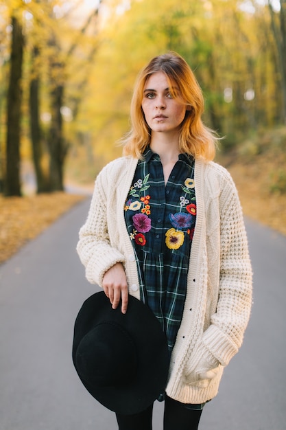 La muchacha elegante del hippie en un suéter y un sombrero hechos punto camina en el parque del otoño.