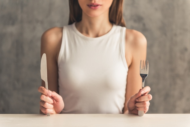 La muchacha está sosteniendo un tenedor y un cuchillo.