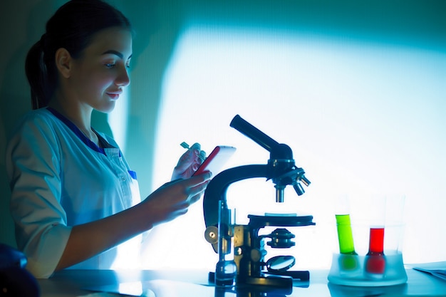 Muchacha del estudiante que mira en un microscopio, concepto del laboratorio de ciencia.