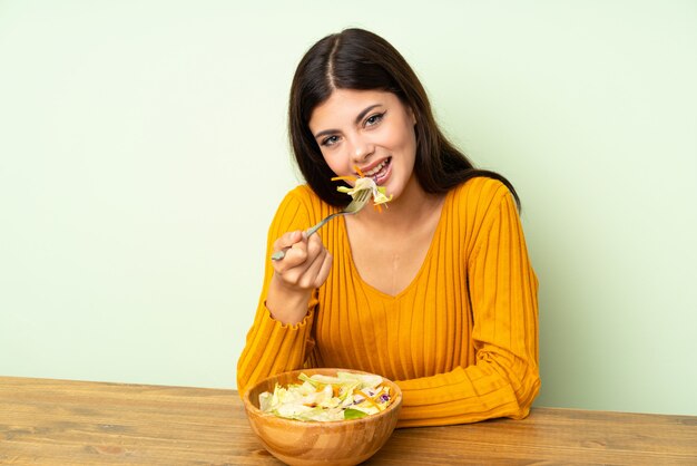 Muchacha feliz del adolescente con la ensalada sobre la pared verde