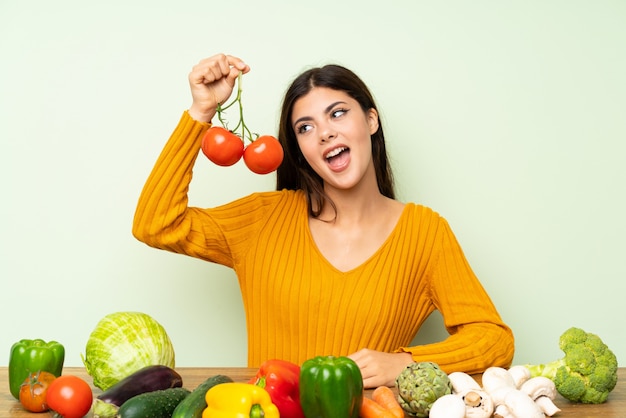 Muchacha feliz del adolescente con muchas verduras sobre la pared verde