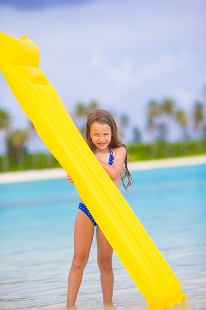 Muchacha feliz adorable con el colchón de aire inflable en la playa blanca