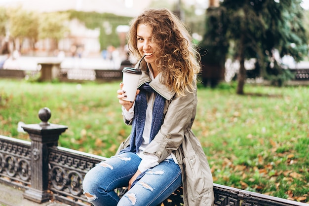 La muchacha feliz con el pelo rizado disfruta de la bebida al aire libre