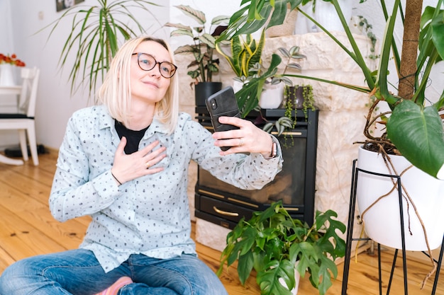 Muchacha feliz que se sienta en la cocina de casa y que sostiene la videollamada. mujer joven con smartphone para videollamada con amigo o familia. seminario web de grabación de vlogger. mujer mirando la cámara y saludando saludando las manos