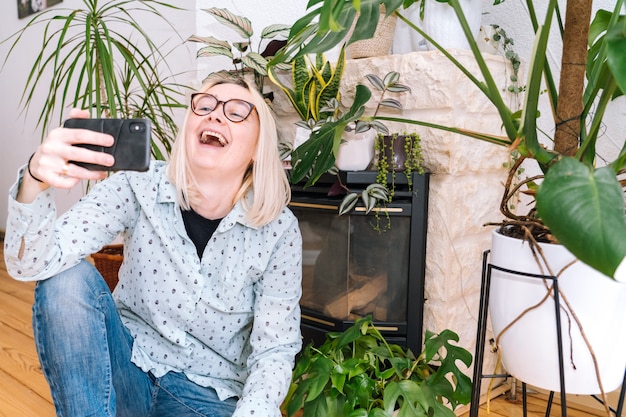 Muchacha feliz que se sienta en la cocina de casa y que sostiene la videollamada. Mujer joven con smartphone para videollamada con amigo o familia. Seminario web de grabación de Vlogger. Mujer mirando la cámara y saludando saludando las manos