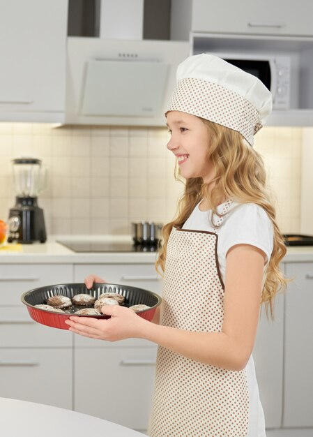 Muchacha feliz que sonríe, sosteniendo la forma de la hornada con las galletas.