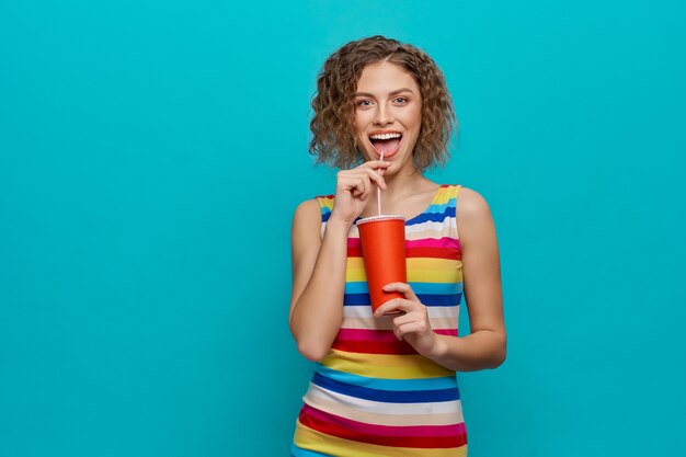 Muchacha feliz que sostiene la taza de papel roja con la paja.