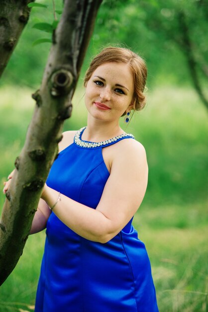 La muchacha gorda joven en el vestido azul presentó el jardín de la primavera del fondo.