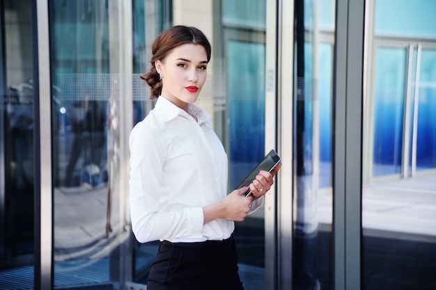 Muchacha hermosa en una camisa blanca en el fondo de un edificio de oficinas