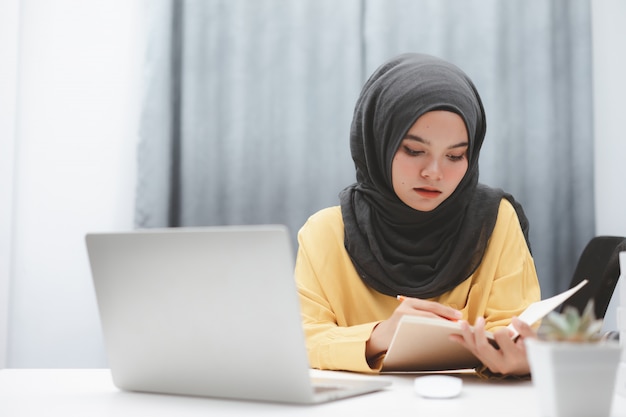 Muchacha hermosa del estudiante musulmán que usa una computadora portátil que aprende en línea en casa. Educación a distancia en línea.