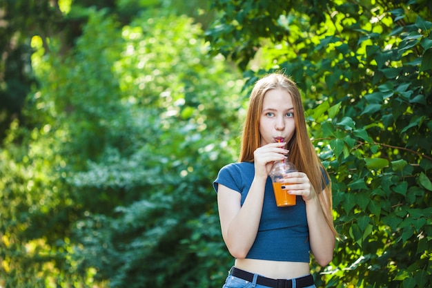 La muchacha hermosa joven bebe el jugo recientemente exprimido en un fondo.