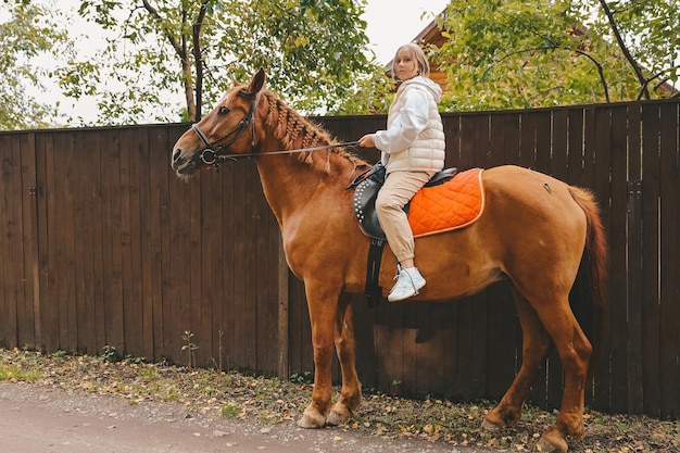 La muchacha hermosa joven monta su caballo a los caminos del país en otoño