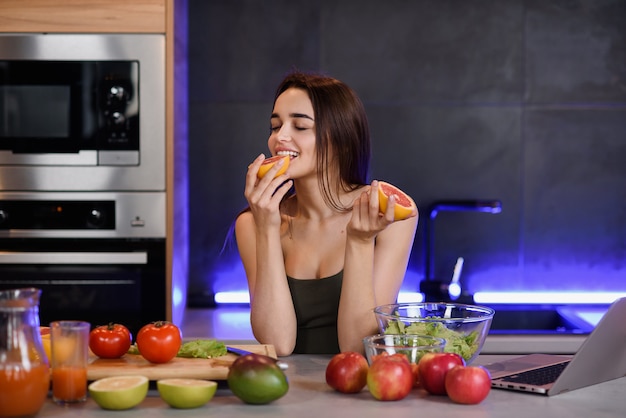 Muchacha hermosa joven que come una naranja, en ropa brillante en un fondo blanco.